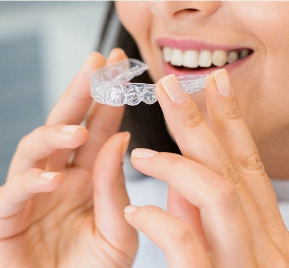 A woman smiling and holding the Invisalign Aligners towards her mouth